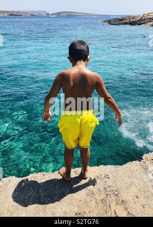 Young boy in bright yellow shorts about to jump into beautiful ocean Stock Photo