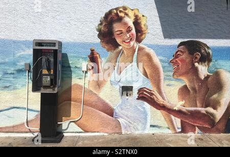 HERMOSA BEACH, CA, JUL 2019: retro soft drink poster artwork, with man resembling Ronald Reagan, painted on wall with payphone outside a store near the beach in Southern California Stock Photo