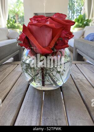 Arrangement of red roses in clear glass vase with water on outdoor table Stock Photo