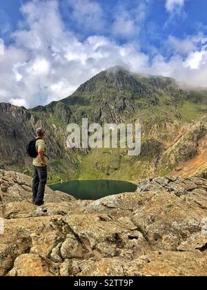 A middle aged man looking up at the cloud capped peak of Snowdon from Glaslyn lake, August. Stock Photo
