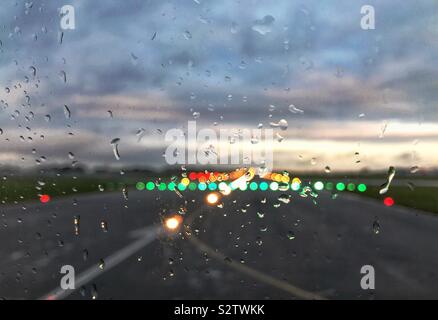 Raindrops on the window of an airliner with the runway lights in the background as it prepares for take-off Stock Photo