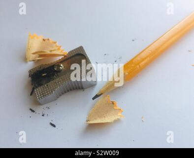 A freshly sharpened yellow pencil, pencil sharpener and pencil shavings. Stock Photo