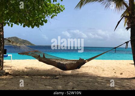 Man in Hammock Relaxing in the Shade Of Two Trees On Palm Island In The Grenadines Stock Photo