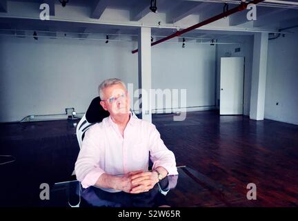 A restful senior man sitting at a desk in an empty office, USA Stock Photo