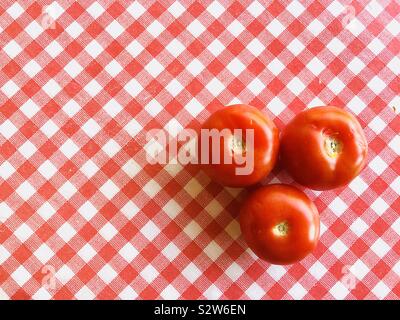 Three large red tomatoes on a red and white checked background Stock Photo