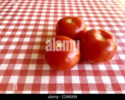 Three large tomatoes on a red and white checked background Stock Photo