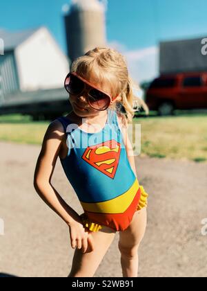 Young girl in red sunglasses and supergirl swimsuit posing with