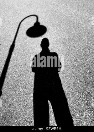 Man under street light silhouetted on pavement Stock Photo