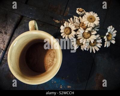 Dusky filter on photo of yellow coffee mug and bouquet of daisies on a blue wooden surface Stock Photo
