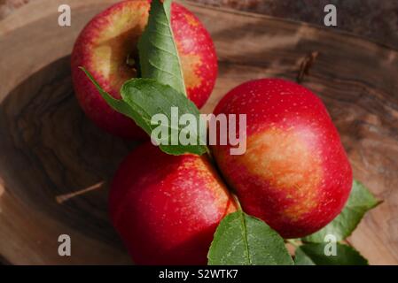 Close up of three red apples on a wooden board with leaves Stock Photo