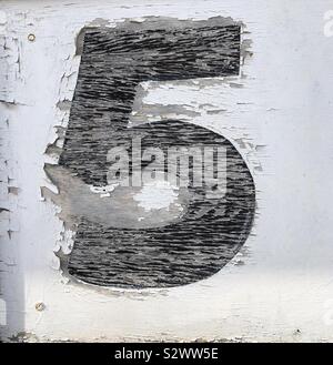 A weathered, cracked, painted number 5 in black on a white background. Stock Photo