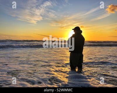 Silhouetted angler fishing at sunset on Llangennith beach, Gower, Swansea, South West Wales, August. Stock Photo