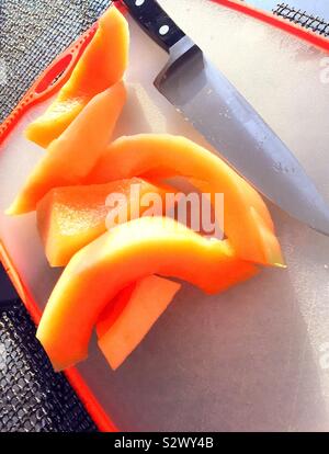 Fresh cantaloupe slices on a cutting board with a prep knife Stock Photo