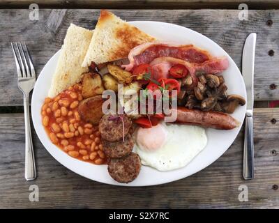 Looking down from above onto a plate full of full English breakfast on the wooden table with knife and fork Stock Photo