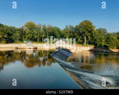 Still water above the weir on The River Taff at Radyr near Cardiff. On the far bank are the buildings of hydroelectric scheme Stock Photo