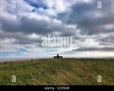 Young woman sitting on a bench looking at the sea and the sky. Stock Photo