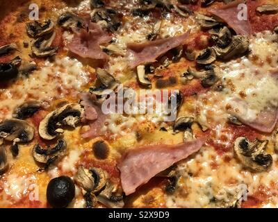 Close up view of a pizza with ham, cheese, mushroom and olives. Stock Photo