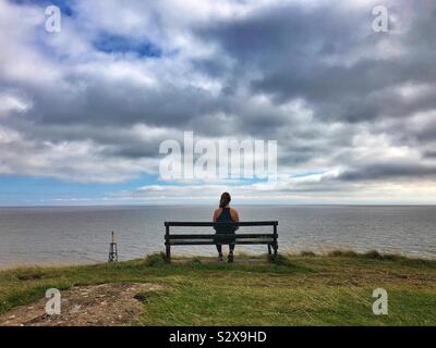 Young woman sitting on a bench enjoying the view over the sea. Stock Photo