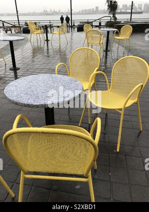 Colourful empty chairs and tables on a grey rainy day in north Vancouver with a view of the waterfront. Stock Photo