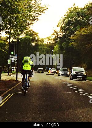 A cyclist with high visibility clothing, on a busy road with trees Stock Photo