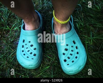 Pair of person’s feet wearing green crocs plastic sandals Stock Photo