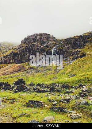 Waterfall falling from misty mountains with building remains in foreground Stock Photo