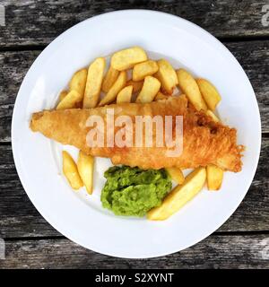 Looking down from above onto a plate full of fish and chips with mushy peas and copy space Stock Photo