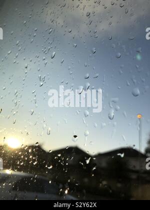 Close up of rain on a window at sunset  overlooking a car park, street light and houses Stock Photo