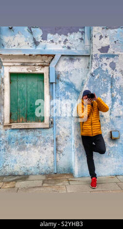 Photographer leaning against a colourful wall in Burano Italy with a green shuttered window Stock Photo