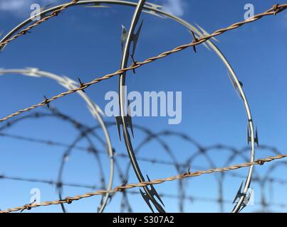 Barbed and razor wire are shown up close, atop a fence, providing security for a secure area. Stock Photo
