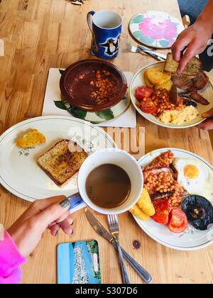 Full English breakfast on the kitchen table. Fried in olive oil bread, mushrooms, hash browns, beans, eggs, tomatoes, sausages, scrambled eggs, coffee and tea.Homemade cooked breakfast for two. London Stock Photo