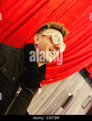 Man wearing sunglasses looking up with red curtain in the background Stock Photo