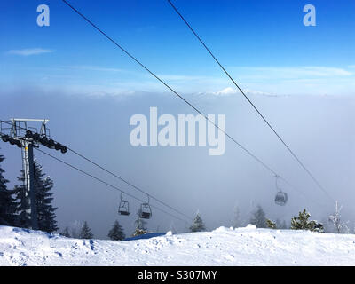 A ski cable car emerges from the fog above the snow-covered mountain top and meets the funicular cabin, which is on the way down into the valley. Stock Photo