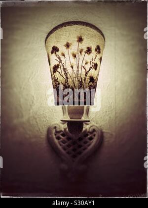 Still life: A grungy photo of an old-fashioned lit wall lamp wit flowery shade in sepia tone casting a warm light.