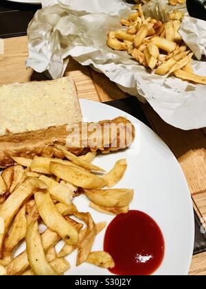 Chip shop style chips and battered sausages eaten at home on a table Stock Photo