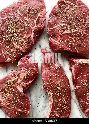Uncooked, seasoned sirloin steaks on a white marble cutting board Stock Photo
