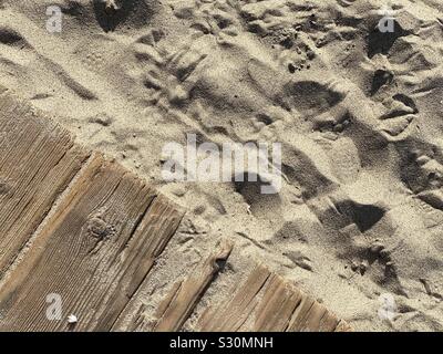 Detail of sandy beach with footprints and bird tracks, next to wooden planks forming boardwalk, creating natural background texture Stock Photo