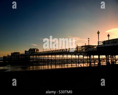 The sun setting behind the pier at Worthing, West Sussex, England, UK at low tide. Stock Photo