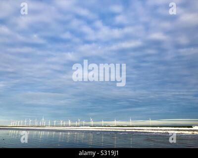 Wind farm off the shore at Redcar reflected in the ebbing tide with a cloud dappled blue sky. Stock Photo