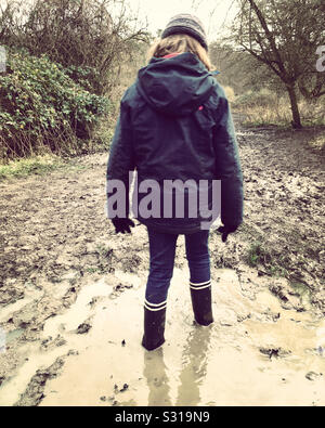 Thoughtful child in water and mud. Girl aged age 7 years stuck in a muddy puddle well wearing Wellington boots. Stock Photo