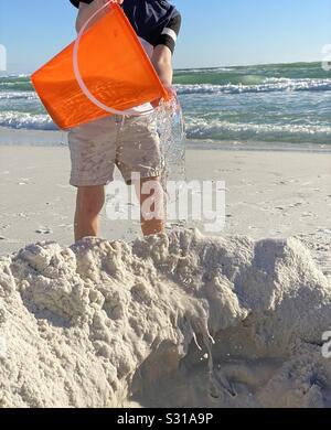 Little boy pouring a bucket of ocean water in a hole in the sand on the beach Stock Photo