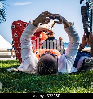 A couple laying on the grass in the sun using their mobile phones Stock Photo