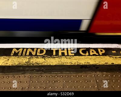 MIND THE GAP sign on the edge of a platform at a London Underground station as a train speeds by. Stock Photo