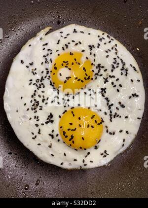 Two fried eggs with black sesame seeds in a frying pan Stock Photo