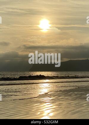 The golden sun sets on a beach in Southern California with low waves rolling in the surf. Stock Photo