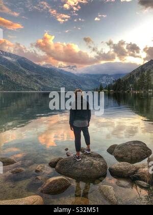 Beautiful lake view with lady standing on a rock taking in the beautiful sunset. Stock Photo