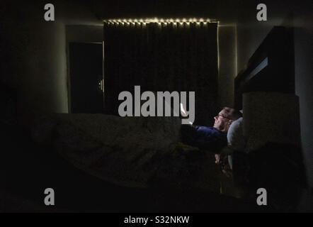 Man reading an ebook from a glowing tablet in a darkened bedroom Stock Photo