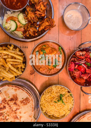 Selection of Indian restaurant food in bowls including chicken tikka masala naan breads rice and fries Stock Photo