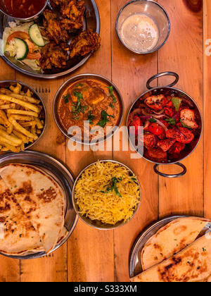 Selection of Indian restaurant food in bowls including chicken tikka masala naan breads rice and fries Stock Photo