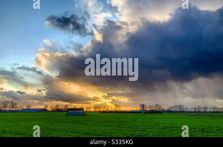 A dark an treathening Storm arises over a sunset farmfield landscape Stock Photo